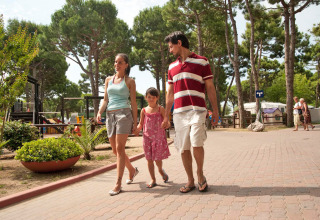 Famiglia che passeggia insieme nel parco vacanze tra gli alberi di Camping Village Cavallino, Veneto, Italia.