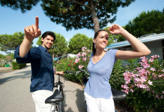 Una coppia felice con biciclette al Camping Village Cavallino in Veneto, circondati da fiori e alberi verdi.