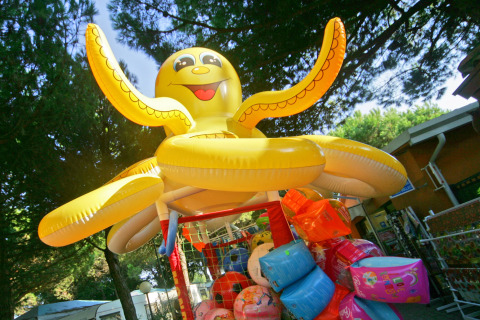 Gran pulpo inflable amarillo y coloridos flotadores junto a árboles en Camping Village Cavallino, Veneto, Italia.