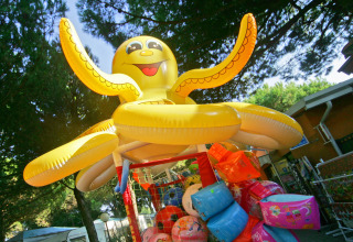 Grande polpo gonfiabile giallo e salvagenti colorati all’ombra degli alberi al Camping Village Cavallino, Veneto.