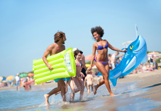 Familie nyder stranden ved Camping Village Cavallino i Veneto med badedyr og oppustelige madrasser.