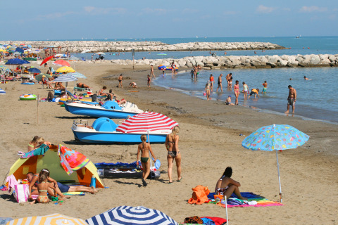 Spiaggia affollata al Camping Village Cavallino in Veneto, Italia, con ombrelloni, bagnanti e pedalò.