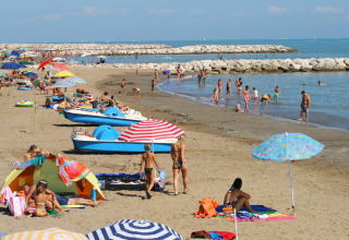 Spiaggia affollata al Camping Village Cavallino in Veneto, Italia, con ombrelloni, bagnanti e pedalò.