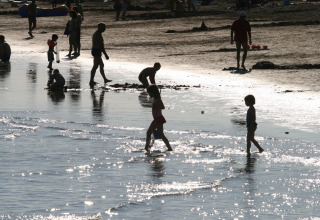 Familier og børn leger ved stranden på Camping Village Cavallino i Veneto, Italien, med sollys på vandet.