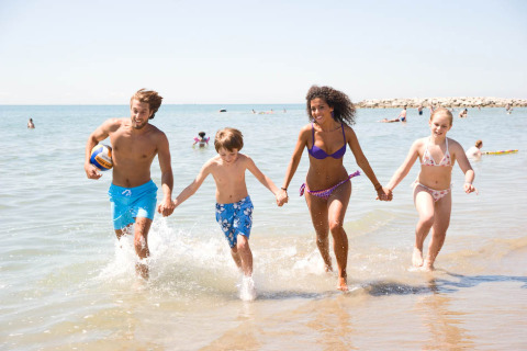 Una familia corre junta por el agua en la playa de Camping Village Cavallino, Veneto, Italia, en un día soleado.