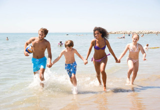 A family runs together in the shallow water at Camping Village Cavallino in Veneto, Italy, enjoying the beach.