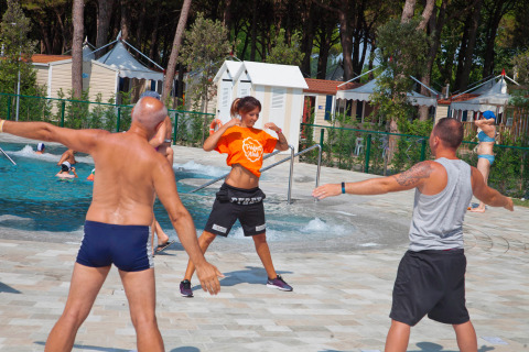 Persone partecipano a una lezione di fitness di gruppo vicino alla piscina al Camping Village Cavallino in Veneto.