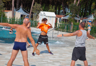 Gruppe mennesker deltager i udendørs fitness ved en pool i ferieparken Camping Village Cavallino, Veneto.