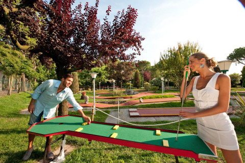 Due persone giocano a mini golf all’aperto al Camping Village Cavallino, parco vacanze in Veneto, Italia.