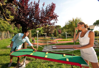 Due persone giocano a mini golf all’aperto al Camping Village Cavallino, parco vacanze in Veneto, Italia.
