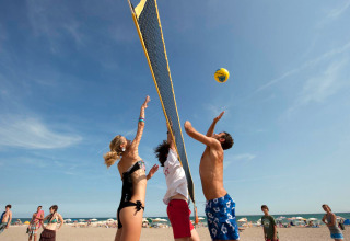 Young people playing beach volleyball under clear blue sky at Camping Village Cavallino in Veneto, Italy.