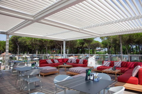 Buitenterras met rode loungebanken en een pergola bij Camping Village Cavallino in Veneto, Italië.