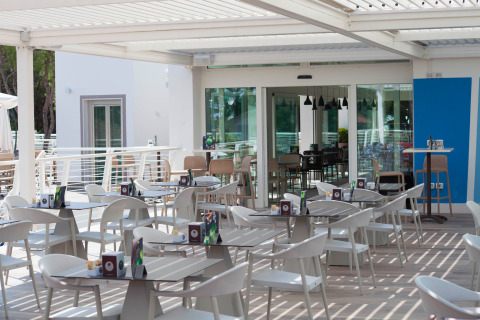 Zona caffè all’aperto con tavoli e sedie bianche moderne al Camping Village Cavallino, Veneto, Italia.