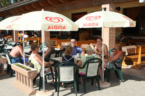 Ospiti del villaggio turistico si rilassano al sole sotto ombrelloni Algida al Camping Village Cavallino, Veneto.