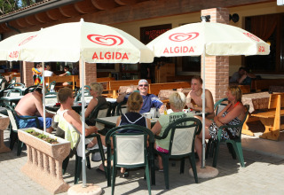 Ospiti del villaggio turistico si rilassano al sole sotto ombrelloni Algida al Camping Village Cavallino, Veneto.