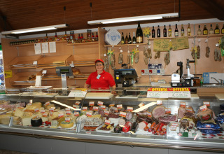 Woman behind deli counter with cheeses and meats at Camping Village Cavallino, Veneto, Italy.