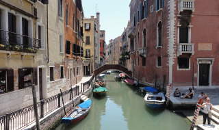 Canal pintoresco con botes y edificios coloridos, personas disfrutando en Cavallino, Véneto, Italia.