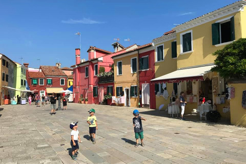 Des enfants jouent sur une place ensoleillée entourée de maisons colorées au Camping Village Cavallino, Vénétie, Italie.