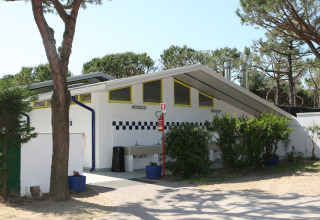 Bâtiment sanitaire extérieur au Camping Village Cavallino en Vénétie, Italie, entouré d'arbres et de verdure.
