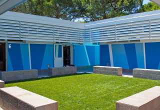 Cortile con prato, panche in pietra e pareti blu al Camping Village Cavallino, Veneto, Italia.
