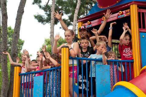 Children and adults wave from a colorful play tower at Camping Village Cavallino holiday park in Veneto, Italy.