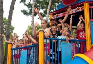 Kinderen en volwassenen zwaaien vanuit een kleurrijke speeltoren bij Camping Village Cavallino, Veneto, Italië.