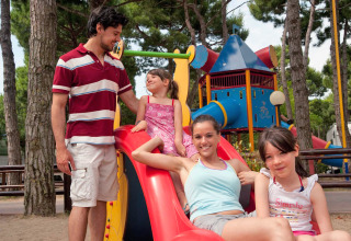Familie nyder tid sammen på legepladsen i Camping Village Cavallino, en feriepark i Veneto, Italien.