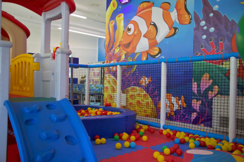 Area giochi interna con scivolo, piscina di palline e murales colorato di pesci a Camping Village Cavallino, Italia.