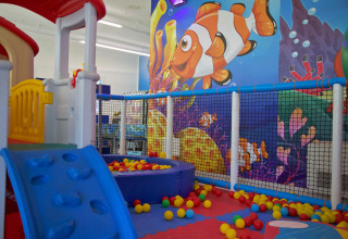 Area giochi interna con scivolo, piscina di palline e murales colorato di pesci a Camping Village Cavallino, Italia.