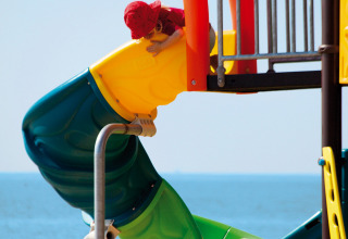Due bambini giocano su uno scivolo colorato vicino alla spiaggia al Camping Village Cavallino, Veneto, Italia.