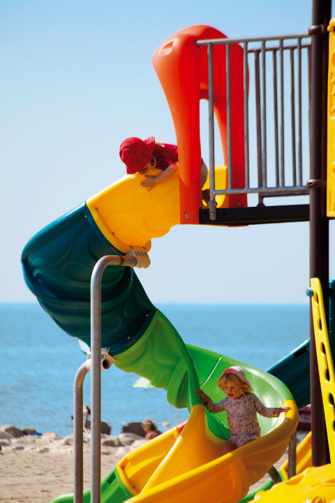Two children play on a colorful playground slide by the beach at Camping Village Cavallino, Veneto, Italy.