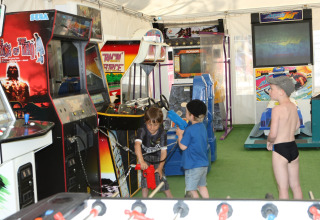 Bambini giocano con i videogiochi arcade nella sala giochi di Camping Village Cavallino, Veneto, Italia.