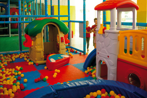 Indoor play area at Camping Village Cavallino, Italy, featuring colorful playhouses, slides, and plastic balls.