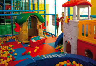 Indoor play area at Camping Village Cavallino, Italy, featuring colorful playhouses, slides, and plastic balls.
