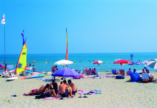 Zonnige dag op het strand bij Camping Village Cavallino, Veneto, Italië, met parasols en watersporters.