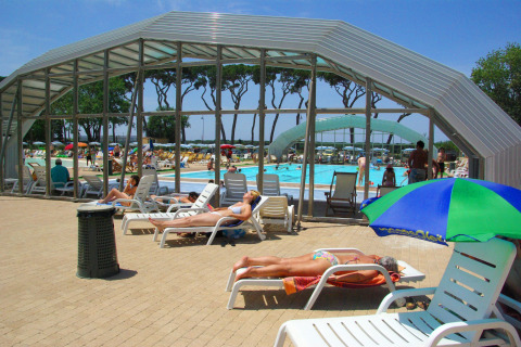 Área de piscina exterior con tumbonas y personas tomando el sol en hu Park Albatros Village, Toscana, Italia.