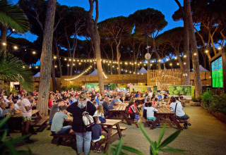 Groep mensen kijkt buiten naar een voetbalwedstrijd op groot scherm bij hu Park Albatros Village in Toscane.