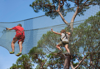 Two people climbing on nets among treetops under blue sky at hu Park Albatros Village, Tuscany, Italy.