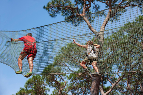 Dos personas trepando redes entre copas de árboles en hu Park Albatros Village, Toscana, Italia.