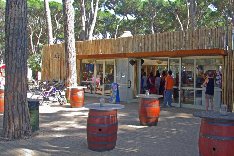 Zona de cafetería al aire libre con mesas de barril y huéspedes en hu Park Albatros Village en Toscana, Italia.