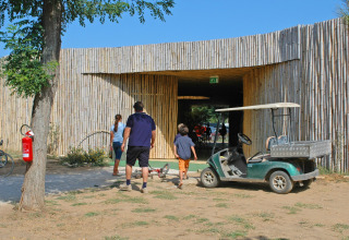 Familie går mod indgangen til hu Park Albatros Village feriepark i Toscana, Italien, med en golfvogn ved siden af.