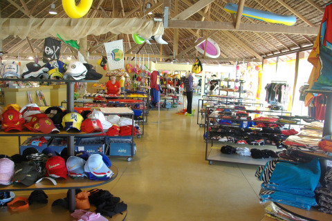 Tienda en hu Park Albatros Village, Toscana, Italia, con ropa, gorros y accesorios bajo techo de paja.