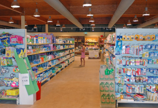 Supermarket aisle at hu Park Albatros Village in Tuscany, Italy, with shelves of products and a shopper.