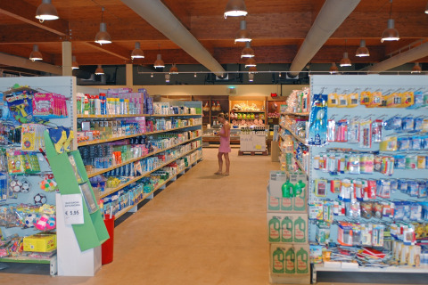 Supermarket aisle at hu Park Albatros Village in Tuscany, Italy, with shelves of products and a shopper.