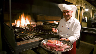 Cocinero con uniforme blanco asa carne sobre fuego en hu Park Albatros Village, parque vacacional en Italia.