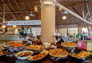 Mesa buffet con diversos platos y salsas bajo techo de paja en hu Park Albatros Village, Toscana, Italia.