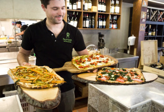 Man serving rustic pizzas on wooden boards at a restaurant in hu Park Albatros Village, Tuscany, Italy.