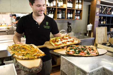 Hombre sirviendo pizzas rústicas sobre tablas de madera en un restaurante de hu Park Albatros Village, Toscana, Italia.