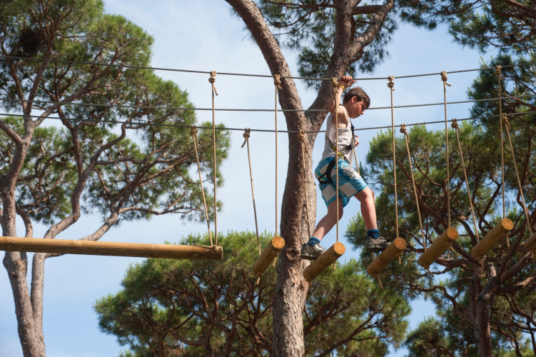 Enfant équipé d’un harnais traverse un parcours aventure en hauteur à hu Park Albatros Village, Toscane, Italie.