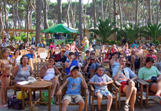 People relaxing outdoors at hu Park Albatros Village holiday park in Tuscany, Italy, among trees and chairs.